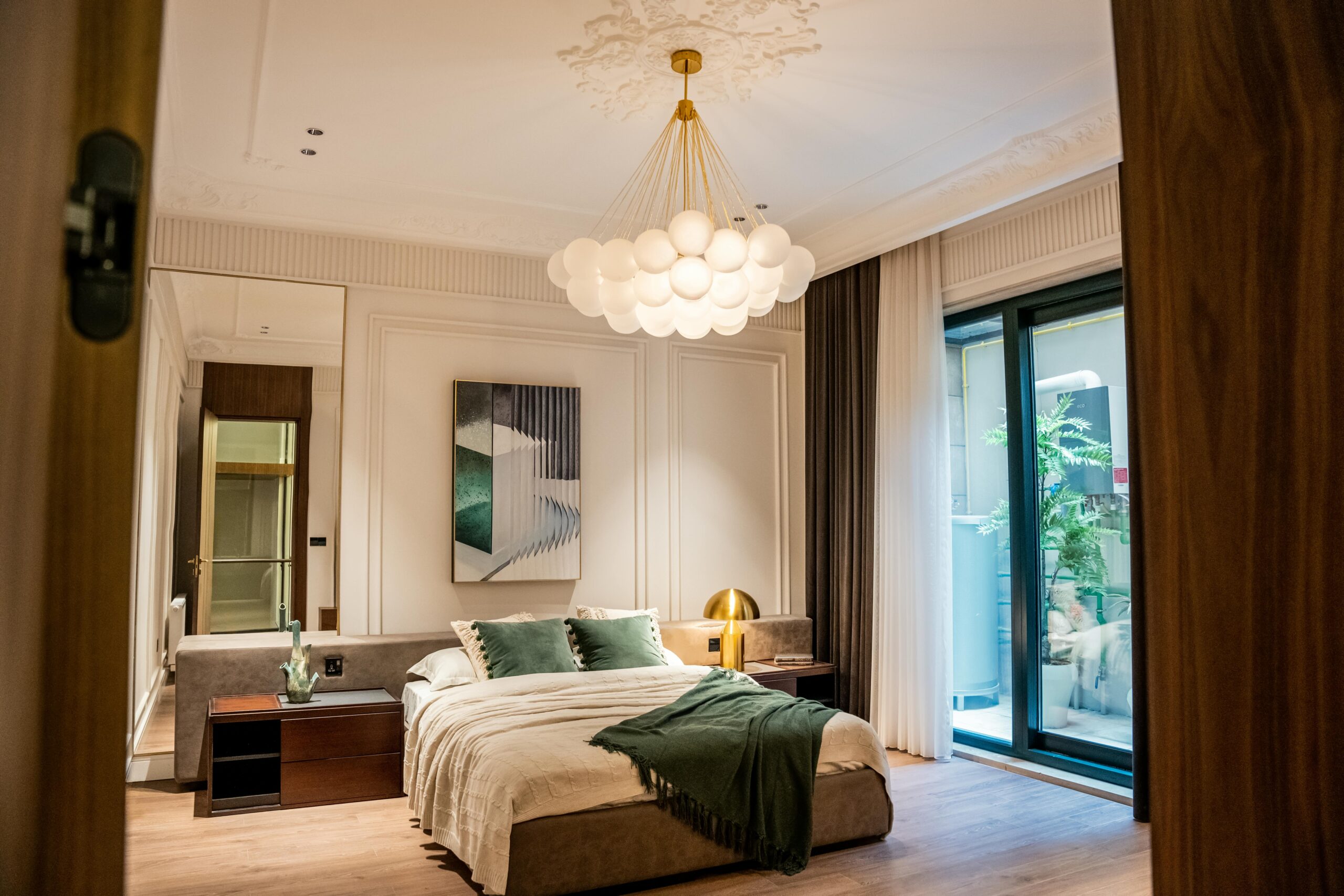 Modern and elegant bedroom featuring green accents, luxurious decor, and a statement chandelier.