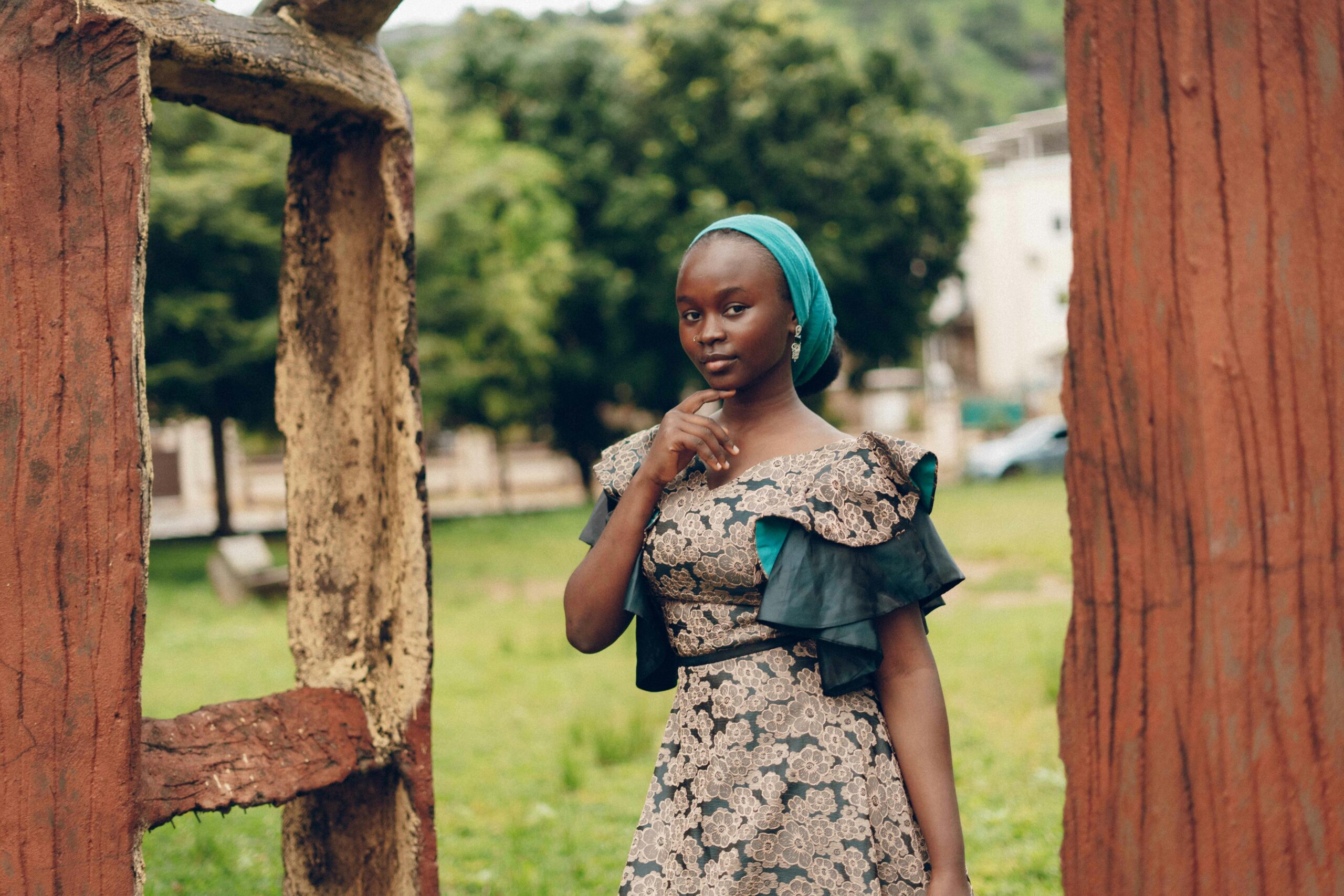 A beautiful Nigerian woman in traditional dress poses gracefully outdoors surrounded by nature.